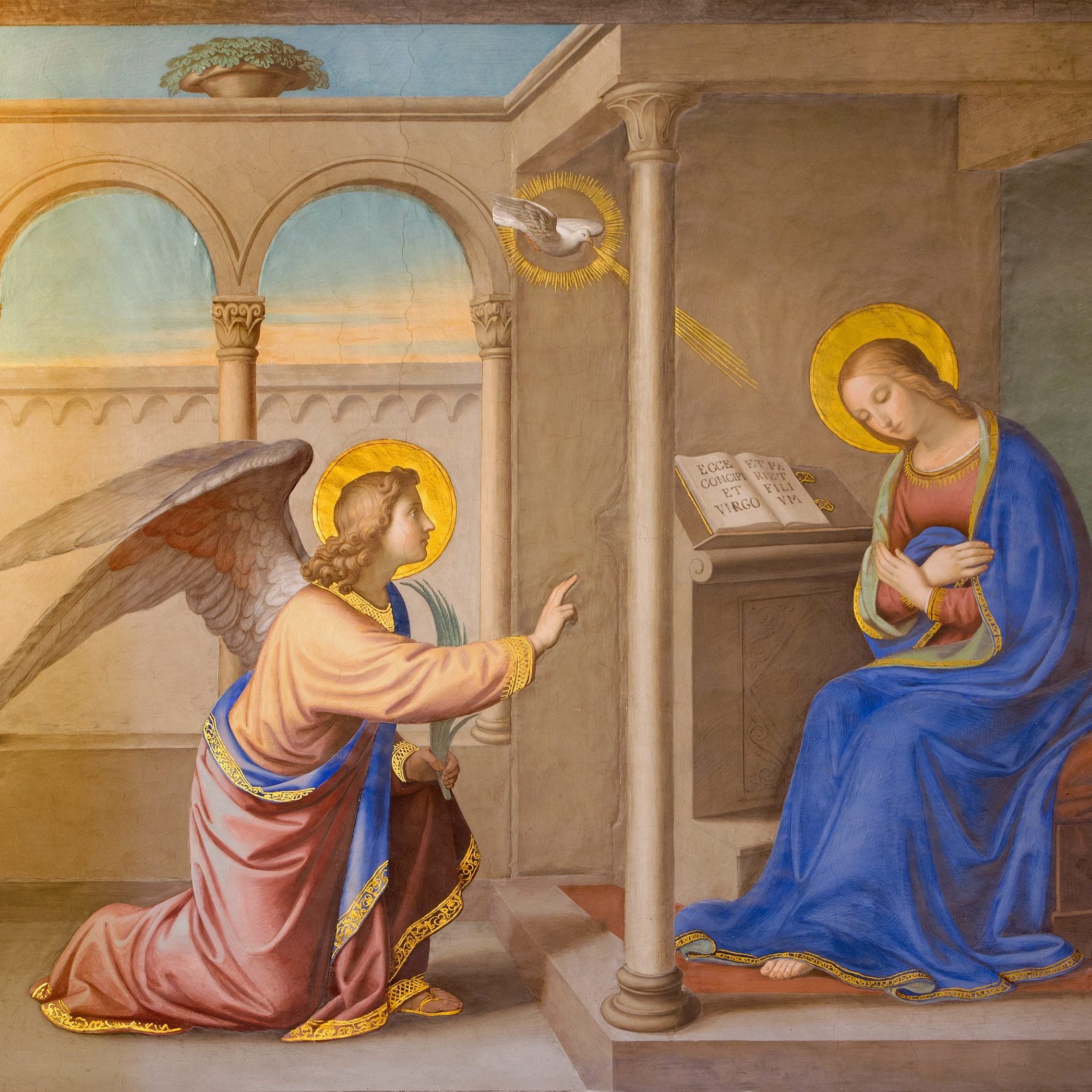 A religious painting depicting the Annunciation, featuring the Angel Gabriel kneeling and speaking to the Virgin Mary, who is seated and holding a small object. A dove representing the Holy Spirit is shown above, and a scroll with text is visible on a nearby lectern.